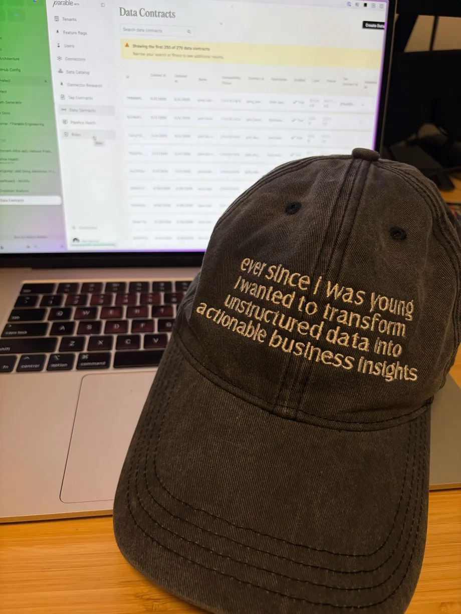 A Parable cap reading "ever since i was young i wanted to transform unstructured data into actionable business insights", resting against a laptop running Parable.